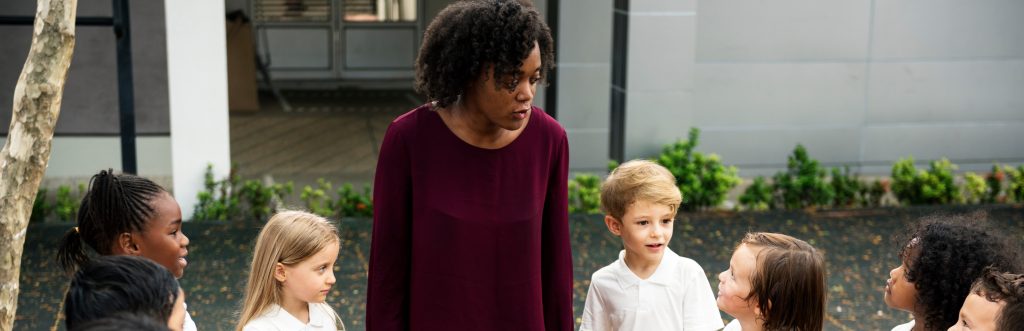 Image of Black woman with children outside school